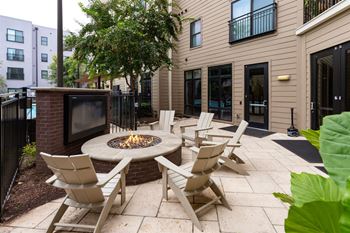 A patio with a fire pit and chairs.